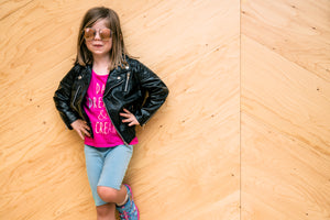 An older girl wearing a pink t shirt black jacket and sunglasses poses with her hands on her hips