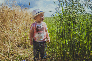 Toddler boy wearing a straw hat walks through a summer field of corn and long grass