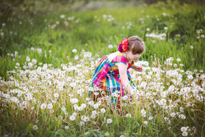 A young girl in a pink dress with a flower in her hair is in a meadow and picking white flowers