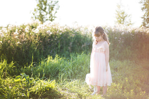 A young girl wearing a pretty pink fairy dress standing outside on green grass